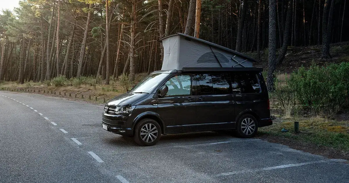 Black campervan with pop-top roof parked beside a forest road, showcasing a peaceful outdoor camping scene and van life travel lifestyle.