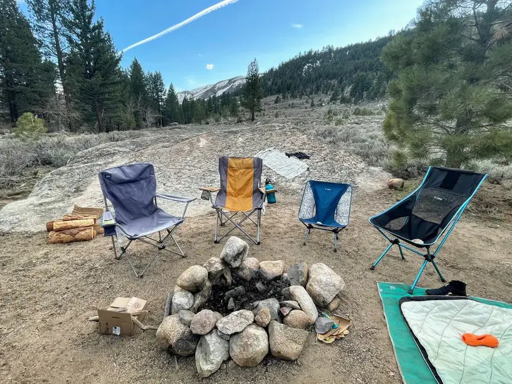 Collection of camping chairs arranged around a stone campfire with mountain and forest views, showing an outdoor seating setup ideal for van life and off-grid camping adventures.