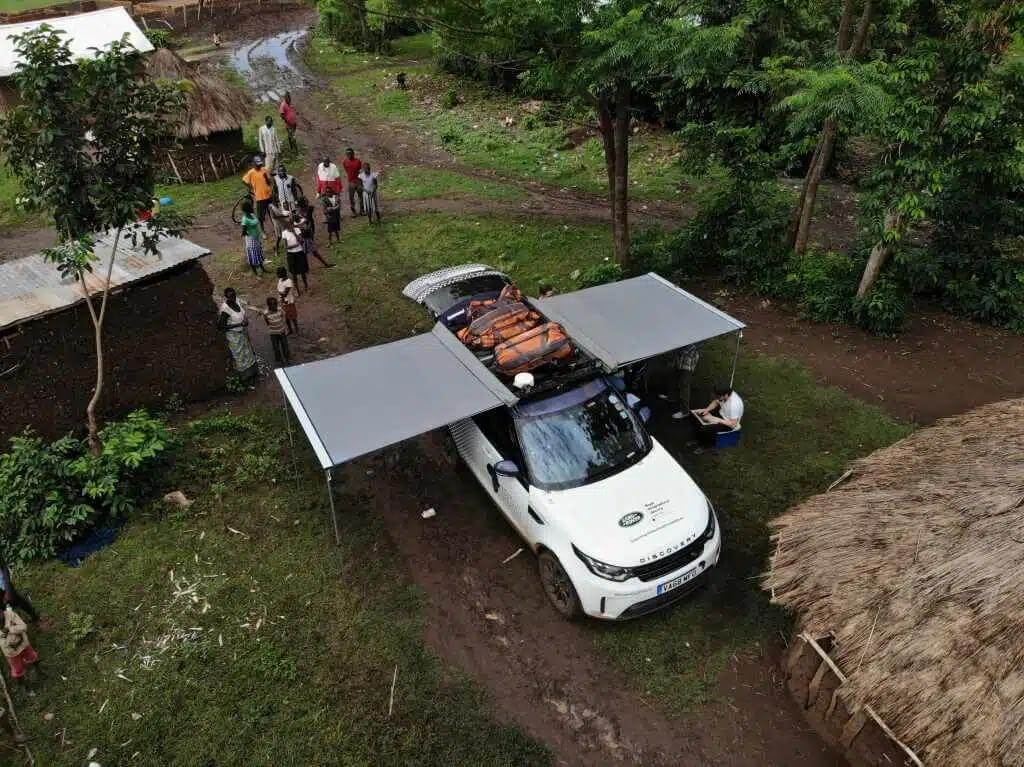 Overhead view of a Land Rover Discovery fitted with awnings and roof gear, parked in a rural area during an overland expedition.