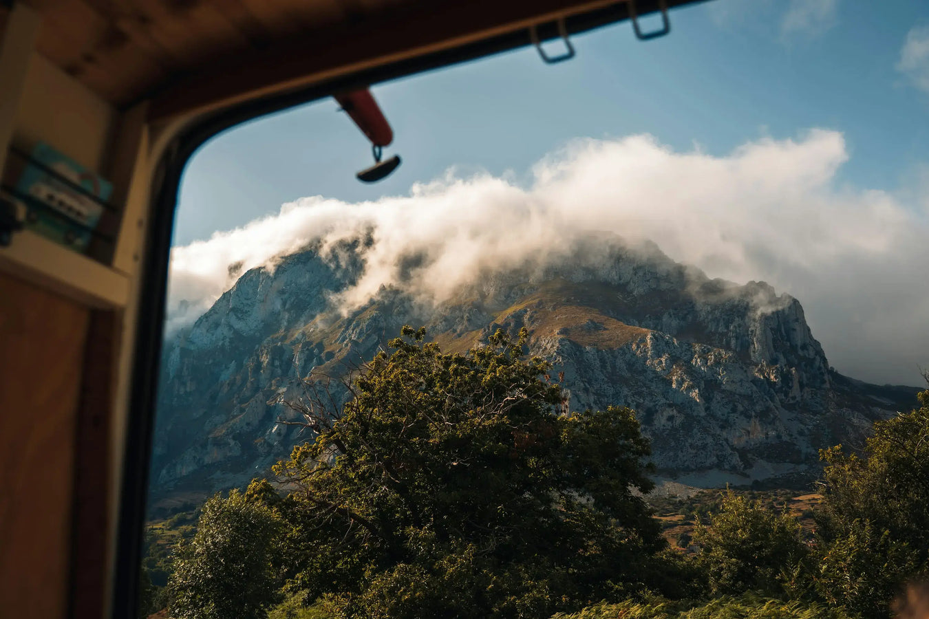 Scenic mountain view with clouds drifting over rocky peaks, seen through a campervan door — capturing the spirit of van life adventure.