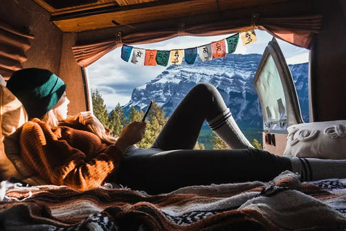 Woman relaxing inside a cosy campervan with mountain views, wrapped in blankets and enjoying the van life experience.