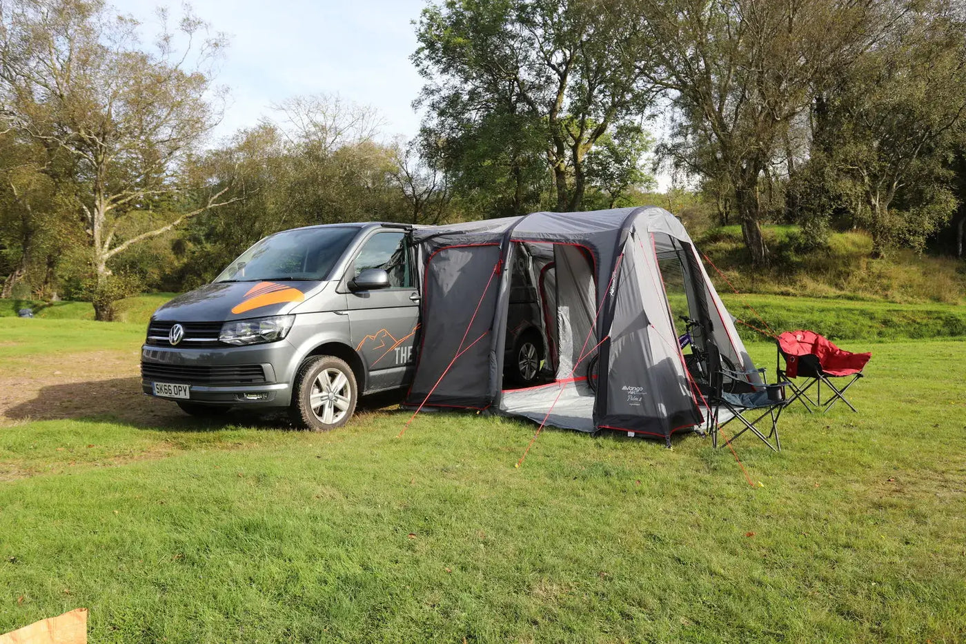 Volkswagen campervan parked with a Vango Faros II Air awning attached on a grassy campsite, showing a compact drive-away setup with outdoor chairs and a relaxed camping environment.