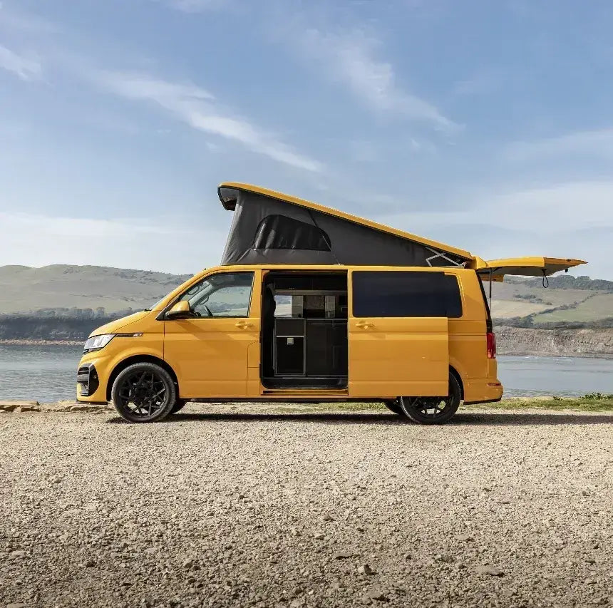 Bright yellow campervan with an open pop-top roof parked beside the sea, showcasing coastal van life travel and outdoor adventure freedom.