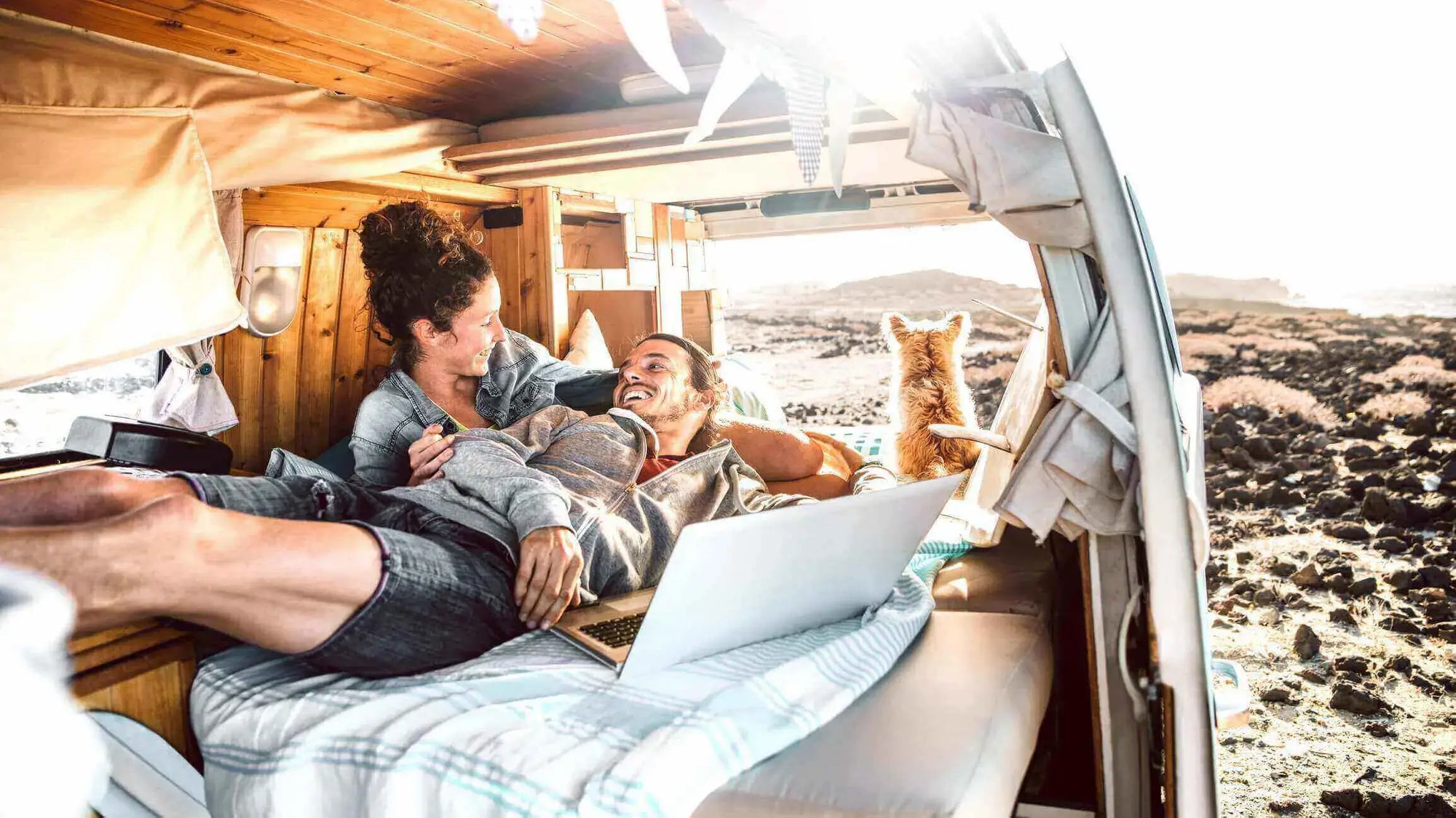 Couple relaxing inside campervan with dog and laptop overlooking the coast — modern van life inspiration.