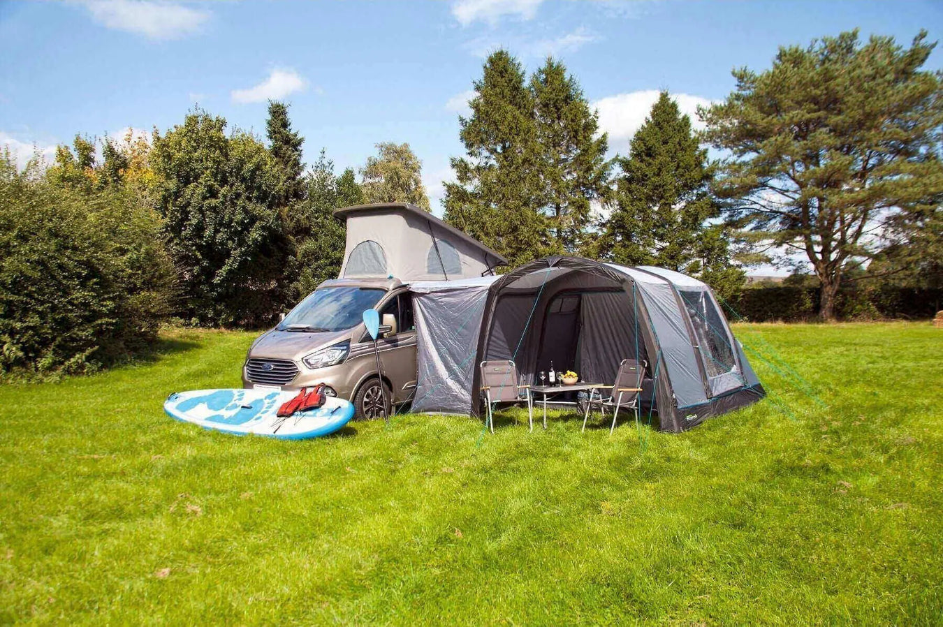 Campervan with inflatable awning and paddleboard set up on a green field — perfect for outdoor camping and van life adventures.