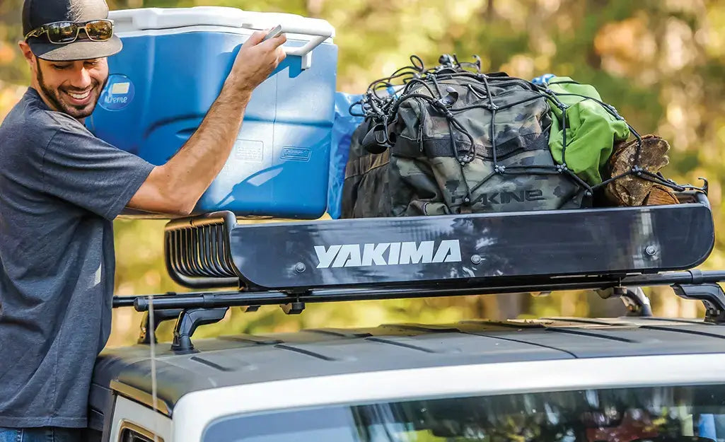 Man loading a blue cooler onto a roof rack packed with camping bags and outdoor gear, showing a van life travel setup.